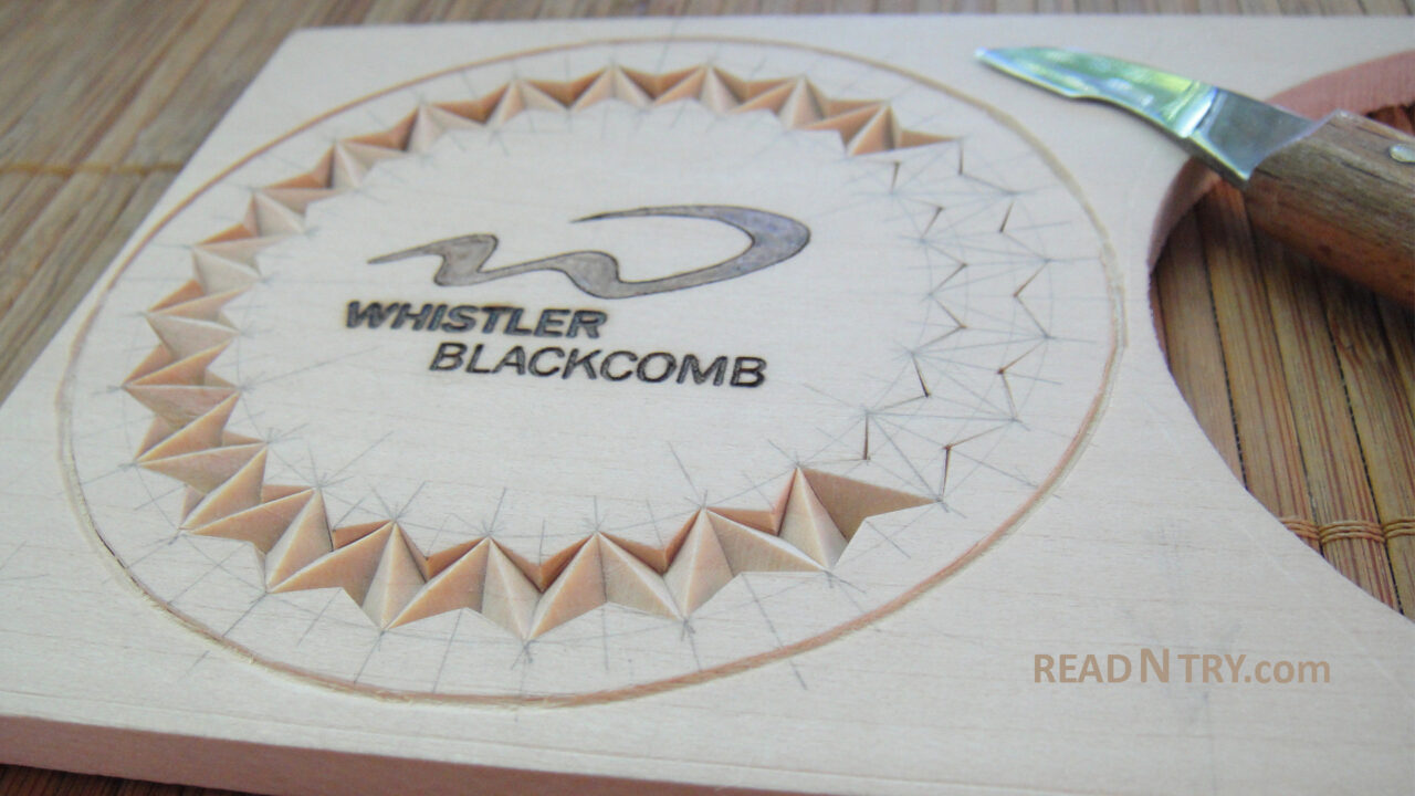 A close-up of a partially chip-carved coaster. A blade from a small chip-carving knife is visible in the image.