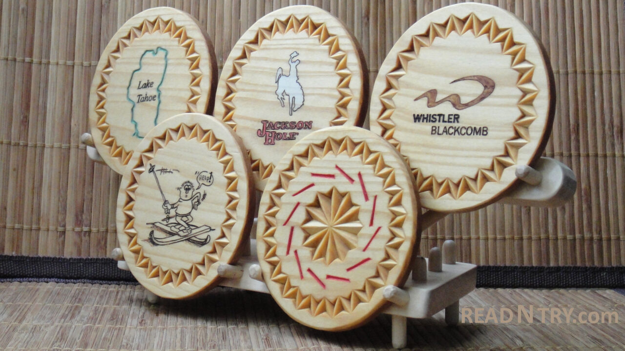 Five chip-carved and winter-theme decorated wooden coasters on a stand. The stand arranges the coaster in the Olympic Rings shape.