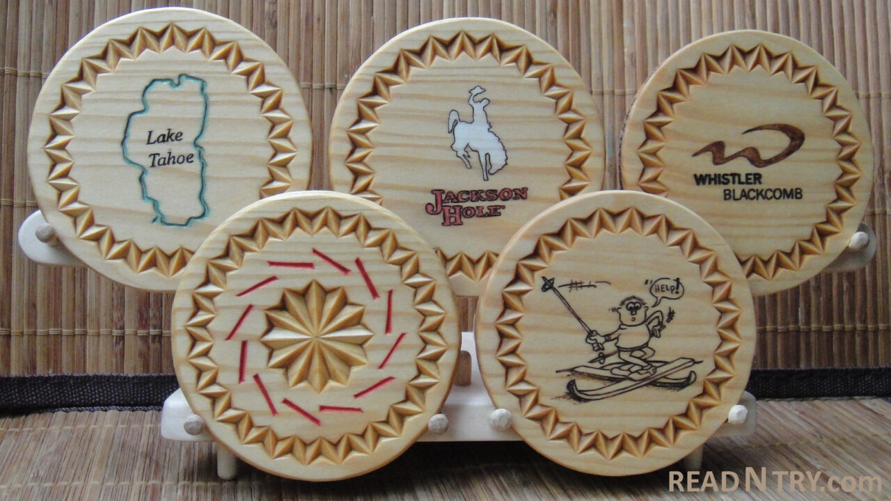 Five chip-carved and winter-theme decorated wooden coasters on a stand. The stand arranges the coaster in the Olympic Rings shape.