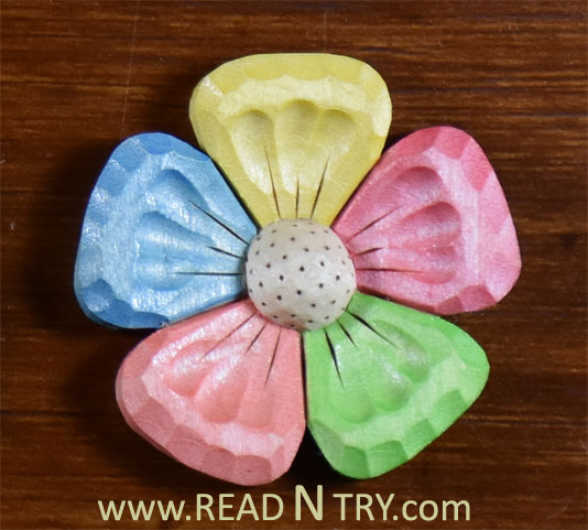 A picture of a carved flower magnet with 5 petals. Each petal is painted in a different color.