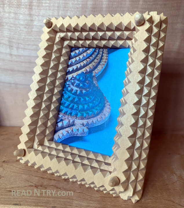 A wooden picture frame carved in the Tramp Art style from basswood. The frame consists of three layers with carved notches.